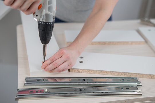 A Caucasian woman uses a screwdriver to tighten a screw while assembling a cabinet.