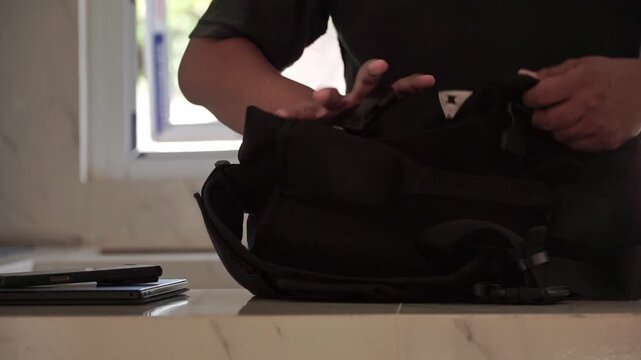 A man organizing a backpack by storing a tablet and smartphone. Digital nomad lifestyle, portable technology, commuting, and productivity concept.