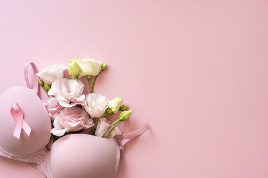 Pink bra with ribbon and fresh flowers on soft pink background for Breast Cancer Awareness month showing feminine support and hope