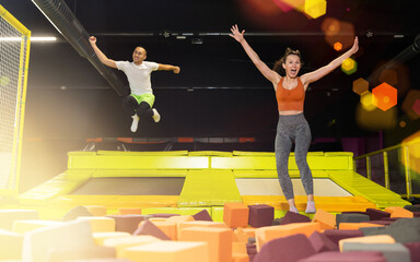 Fototapeta premium Happy excited middle-aged woman playfully jumping into colorful foam cube pit at lively indoor trampoline park
