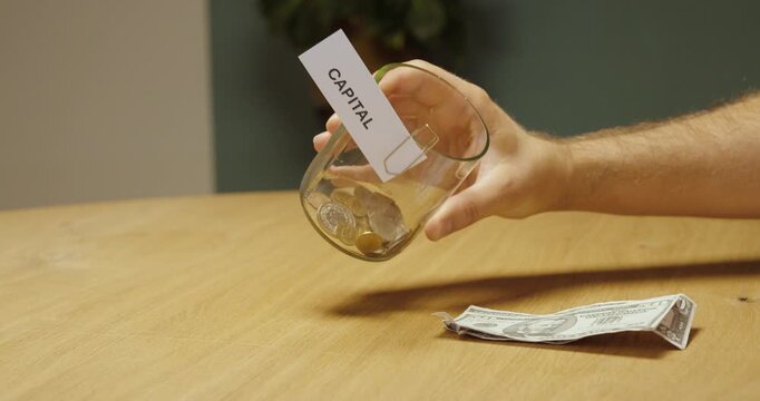 Person checking a jar labeled &ldquo;Capital&rdquo; with money nearby, representing capital assessment, available funds, personal finance and financial planning.