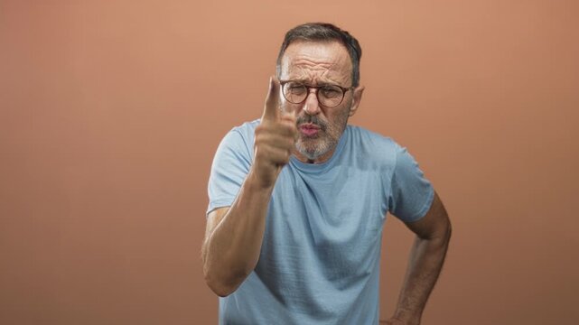 Man pointing finger and scolding with hand on hip in studio against peach backdrop; anger authority.
