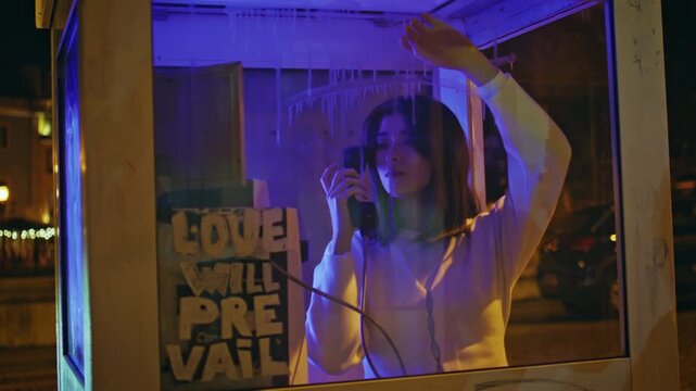 Woman talking payphone booth night city. Girl calling telephone neon street.
