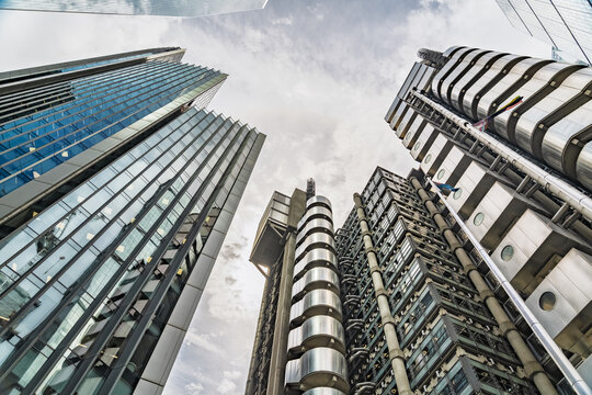 View of the Lloyd's building with its distinctive external service ducts and glass facade, surrounded by modern glass skyscrapers under a cloudy sky in London, England, United Kingdom.