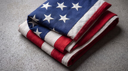 Fototapeta premium Close-up of a neatly folded American flag with stars and stripes, resting on a textured gray concrete background.
