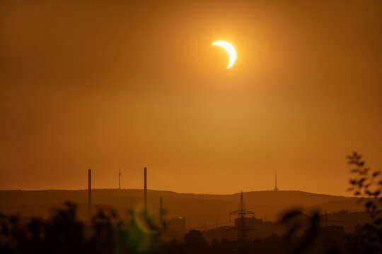 12 August 2026, a partial solar eclipse shines over the city skyline and TV tower in an orange glowing sky, Stuttgart, Germany.