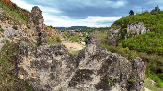 Aerial Close-Up of Tall Rock Spire in Zemen Gorge with Green Valley and Village in Bulgaria