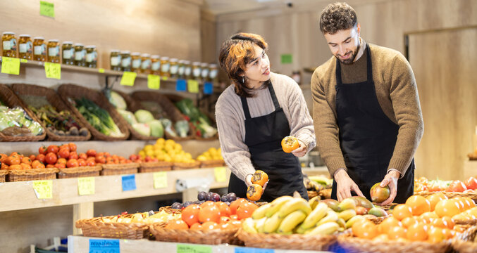 Careful male and female sellers placing persimmons and mangos on product stand in grocery market