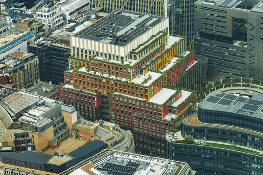 View of a modern building with a stepped design, red and orange facade, and green roof terraces surrounded by office buildings in London, England, United Kingdom.