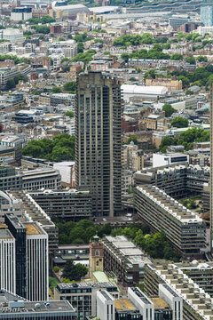 View of the brutalist architecture of the Barbican Estate towers surrounded by residential blocks and lush green trees in London, England, United Kingdom.