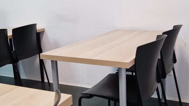 Side view of empty wooden desks and black chairs along the wall in a language school classroom