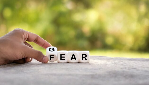 Hand turning a letter block to change the word fear to gear on stone surface