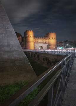 View of the illuminated Pyramid of Cestius and the ancient Porta San Paolo gate at night with light trails from passing traffic in Rome, Lazio, Italy.