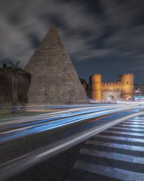 View of the ancient Pyramid of Cestius and the historic Porta San Paolo at night with light trails from passing traffic in Rome, Lazio, Italy.