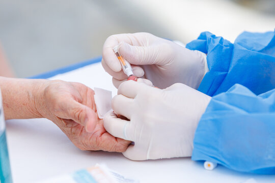 Doctor using safety lancet for capillary blood test prick on senior patient finger