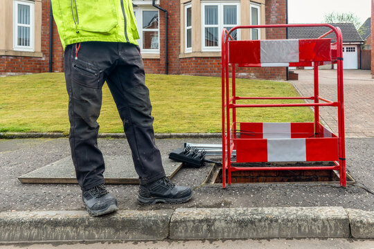 Worker beside open telecoms chamber and barrier on residential street
