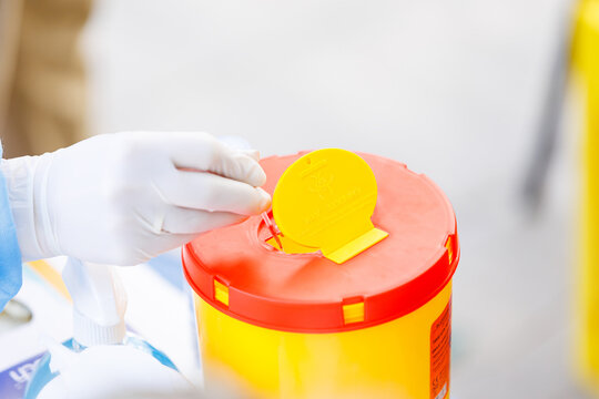 Doctor in gloves disposing used blood capillary tube into biohazard sharps container