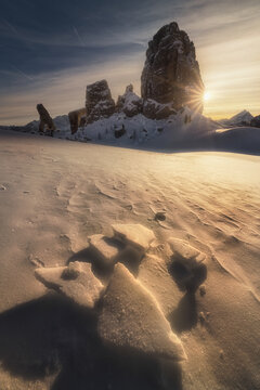 View of the Cinque Torri rock formations during golden hour with snow-covered slopes and ice fragments in the foreground in Cortina d'Ampezzo, Veneto, Italy.
