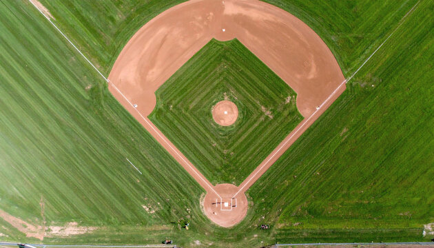 Baseball field aerial view showing a green grass diamond with brown dirt base paths in a sunny outdoor park setting