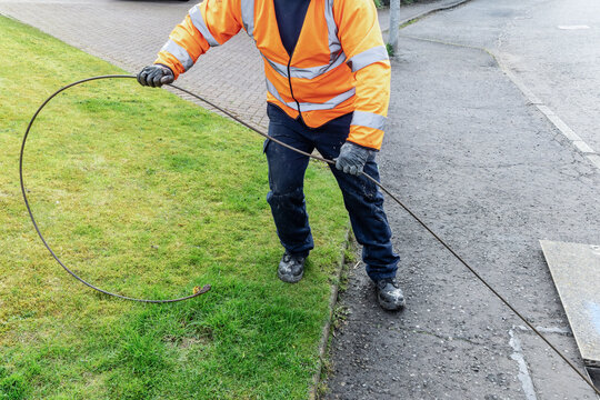 Engineer pulls large loop of cable across grass verge in street
