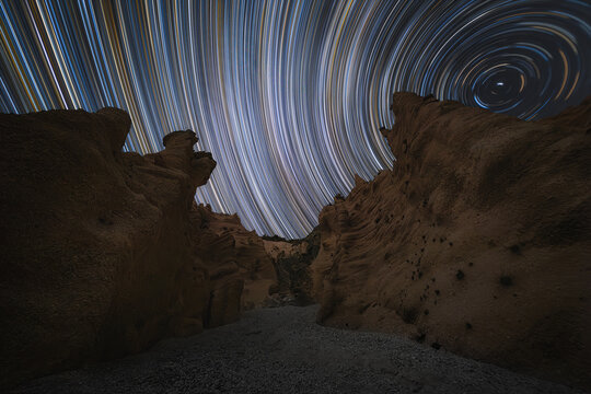 View of the Lame Rosse rock formations under a vibrant star trail night sky in Fiastra, Marche, Italy.