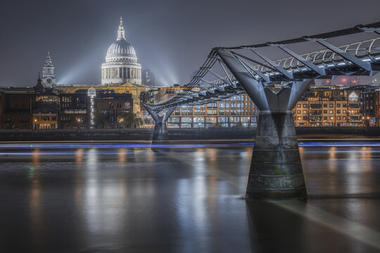 View of the illuminated St. Paul's Cathedral and the Millennium Bridge spanning the River Thames at night in London, England, United Kingdom.