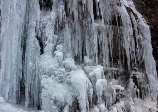 Ice formations cover a rocky surface in a winter landscape near a waterfall in a forest setting