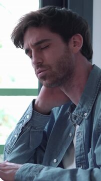 Overworked male freelancer feeling tired and suffering from neck pain due to long hours working on his laptop, massaging his tense muscles to relieve stress and exhaustion at his desk