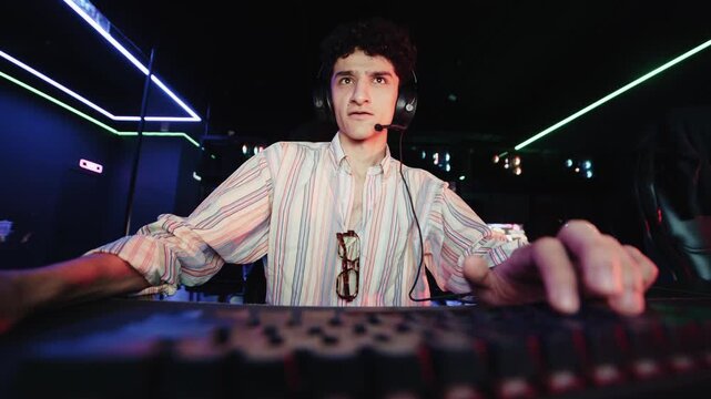 Focused young man playing an online video game in a computer club with neon lights in the background