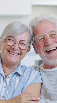 Beautiful and smiling elderly couple enjoying retirement while having fun, talking, and laughing together, relaxing on the couch at home in their living room, sharing a moment of complicity