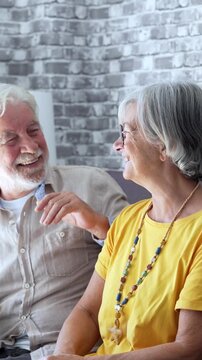 Cheerful caucasian senior couple sitting on the sofa at home, laughing and talking together while enjoying a relaxed retirement lifestyle, showing affection and complicity in their golden years