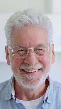 Portrait of a happy senior man with grey hair and a beard, wearing eyeglasses and smiling warmly, showing a positive and cheerful expression while looking directly at the camera