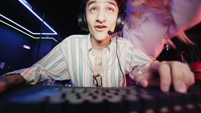 Young man wearing a headset playing an online video game while his girlfriend cheers him on