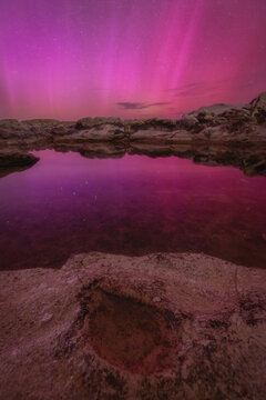 View of the Sedia del Papa rock formation reflecting a vibrant pink aurora in the night sky over the rocky coastline in Ancona, Marche, Italy.