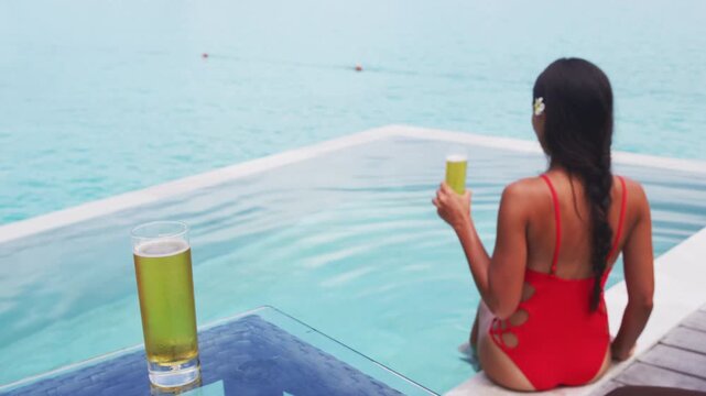 Beers. Woman drinking beer having fun in hotel pool by relaxing and drinking beer. Luxury resort travel vacation concept. Raw unedited video of real unretouched woman model without any makeup