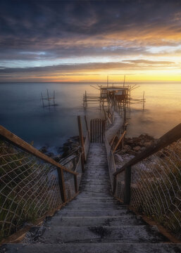 View of the Trabocco Mucchiola, a traditional wooden fishing structure serving as a restaurant, at sunset with calm sea and wooden stairs in Ripari Bardella, Provincia di Chieti, Italy.