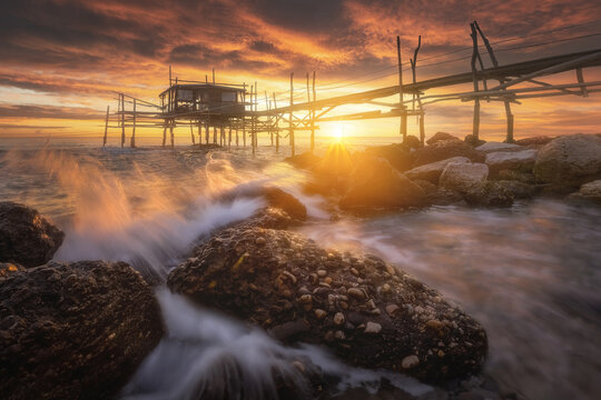 View of the Trabocco Mucchiola restaurant at sunset with waves crashing against the rocky shoreline, Ripari Bardella, Provincia di Chieti, Italy.