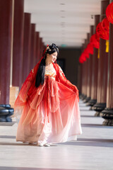 Obraz premium In a traditional hanfu culture photo shoot: a graceful young woman in traditional red Chinese hanfu, sleeve flares right, glances toward the side, beside red pillared temple corridor.