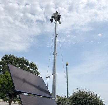 Solar powered mobile security camera trailer with dome cameras, megaphones, solar panels operating in commercial parking lot for crime deterrence