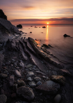 View of the Sassi Neri beach at sunrise with smooth water and rocky coastline in Sirolo, Marche, Italy.