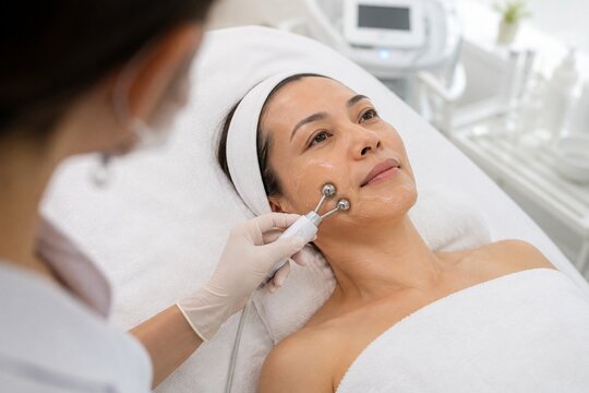 Asian woman receiving microcurrent facial treatment in spa clinic