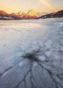 View of the frozen surface of Lake Campotosto with intricate ice patterns and snow-covered mountains illuminated by the golden hour light in Campotosto, Abruzzo, Italy.