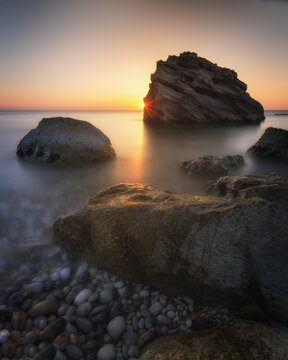 View of large rocks on the pebble beach at sunrise with calm sea and soft golden light in Pedaso, Marche, Italy.