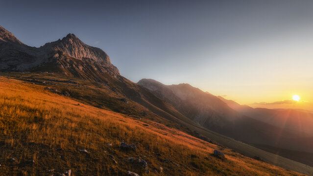 View of Prati di Tivo mountain landscape at sunset with golden light illuminating the grassy slopes and rocky peaks in the Gran Sasso massif, Prati di Tivo, Abruzzo, Italy.