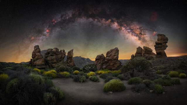 View of the Roque Cinchado rock formation under the Milky Way galaxy in the night sky, with volcanic landscape and sparse vegetation in Santa Cruz de Tenerife, Canary Islands, Spain.