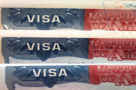 Three United States visa stamp inside an open passport document, held by a hand, for immigration, international travel, border security, visa application, and citizenship topics.