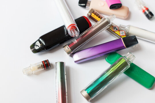 Scattered colorful disposable vapes and pods featuring toxic warning symbols, illustrating nicotine addiction, health hazards, and lung damage caused by modern electronic cigarettes.
