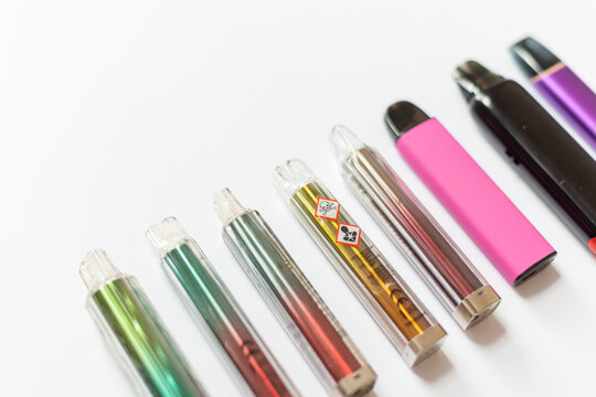Diagonal row of colorful disposable vapes with toxic hazard warnings on a white background, demonstrating chemical health risks, nicotine addiction, and lung damage from electronic cigarettes.