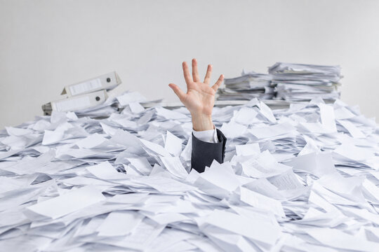 AI generated business hand reaching from huge pile of office paperwork showing work overload stress bureaucracy deadline pressure administrative chaos
