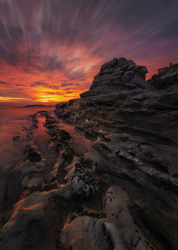 View of the Sedia del Papa rock formation on the Adriatic coast at sunset with long exposure waves washing over the textured shoreline in Ancona, Marche, Italy.